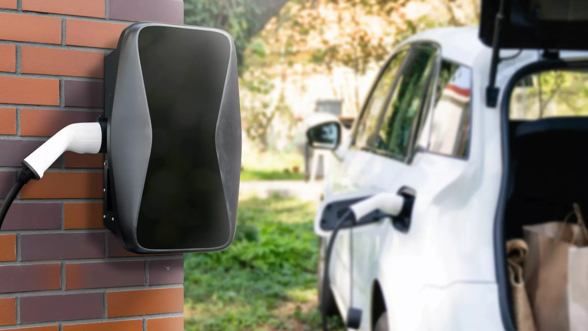 Charging electric car next to house with charging station on the wall